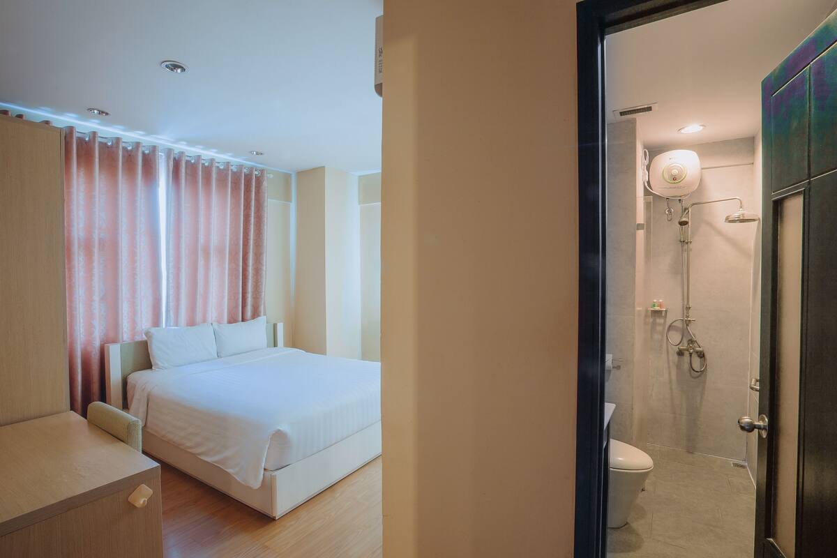 A hotel room with a bed, a bedside table, a shower, and a toilet.