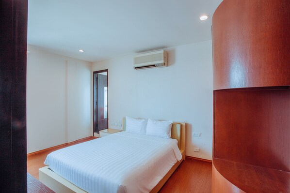 Habitación de hotel con cama, cabecero de madera, aire acondicionado de pared y piso de madera.