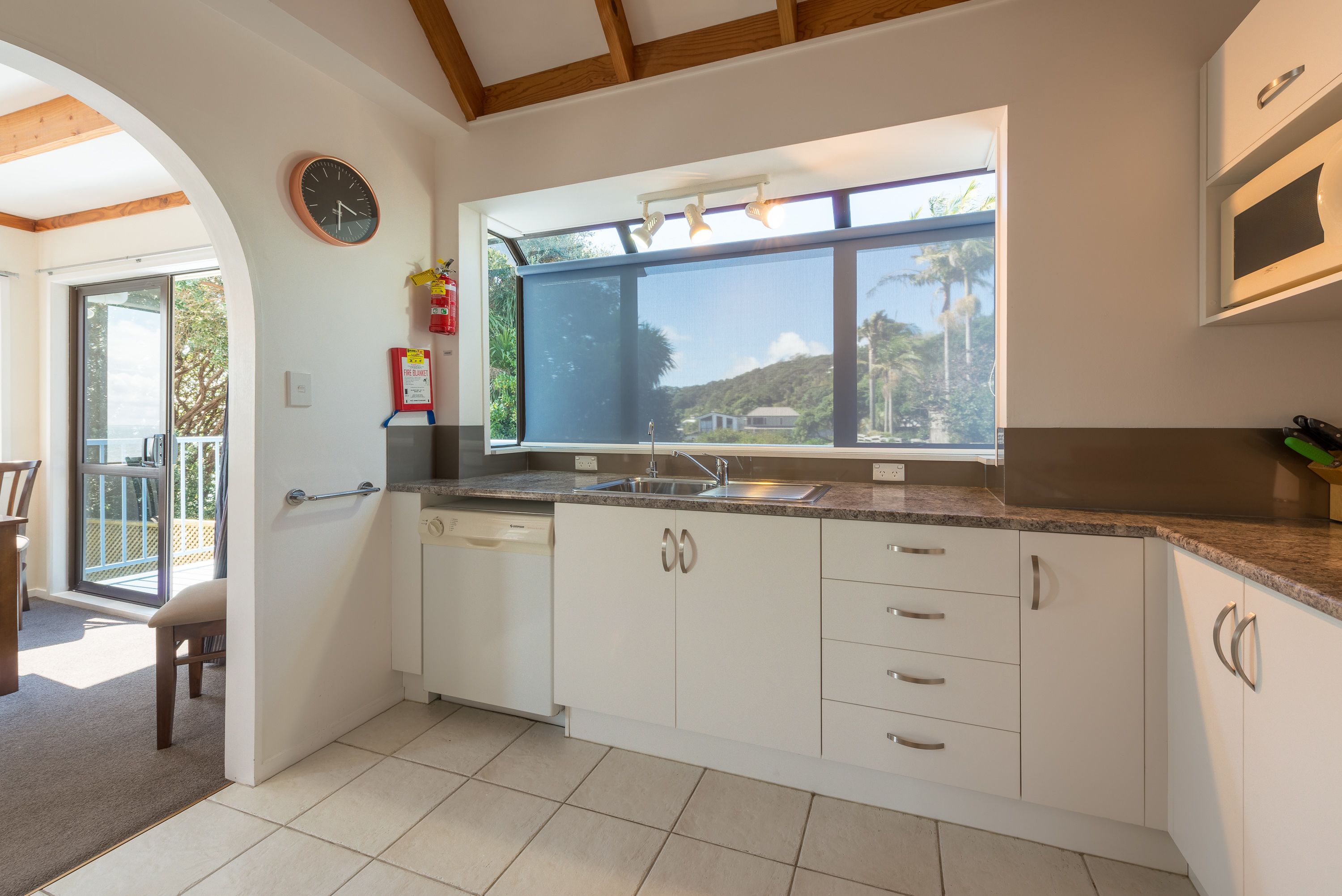 A modern kitchen with white cabinets, a built-in oven, and a large window offering a view of the outdoors.