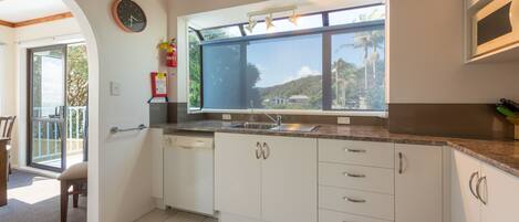A modern kitchen with white cabinets, a built-in oven, and a large window offering a view of the outdoors.