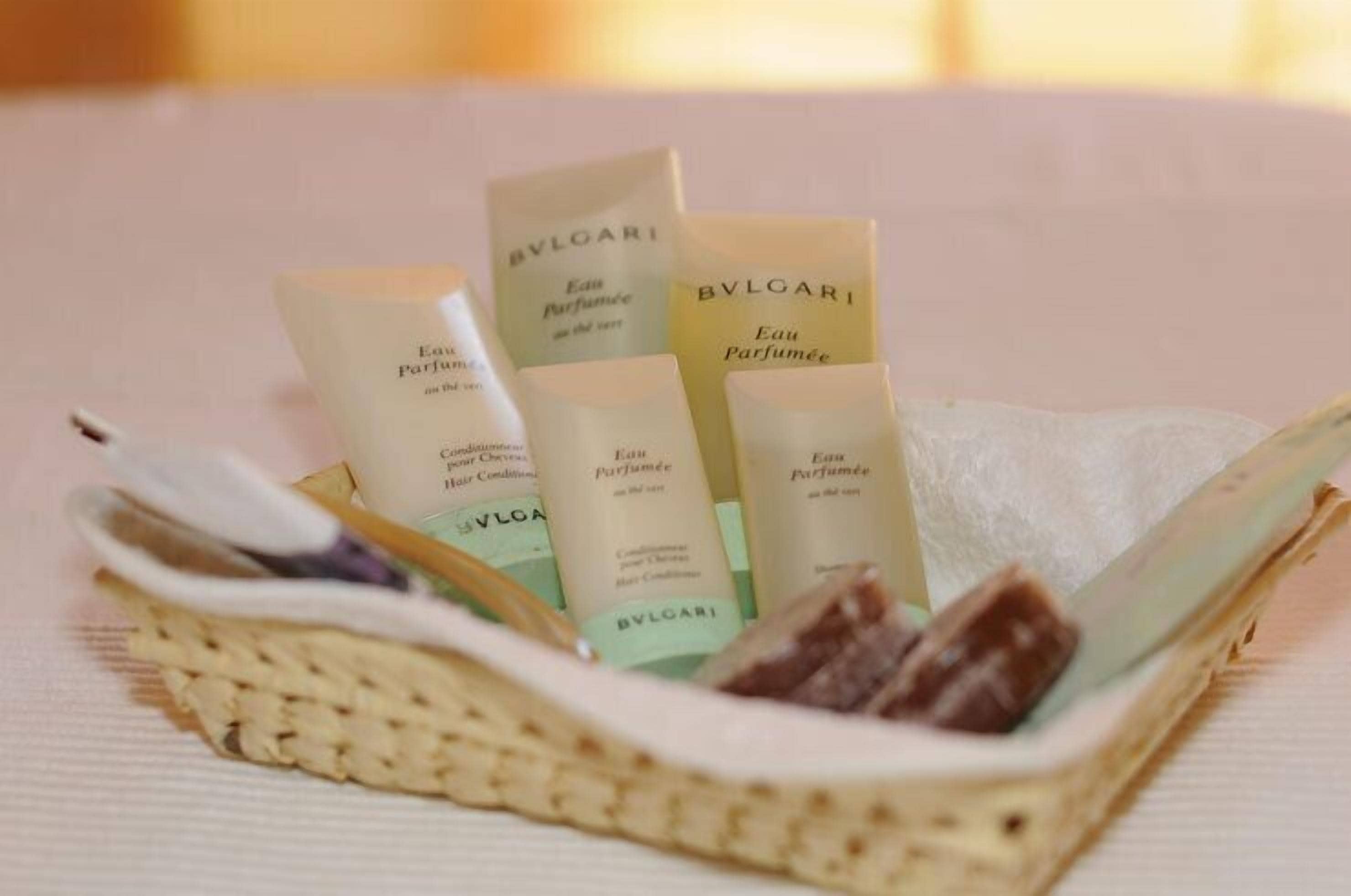 Una cesta de mimbre con varias botellas de Eau de Parfum Bvlgari, un paño blanco y un pequeño objeto marrón.