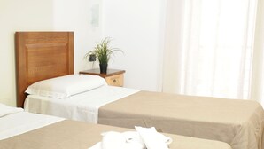 Quarto de hotel com duas camas, cabeceira de madeira, mesa de cabeceira pequena com uma planta e um quadro na parede.