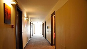 Corredor de hotel com portas em ambos os lados, piso coberto de carpete e luminárias fixadas na parede.