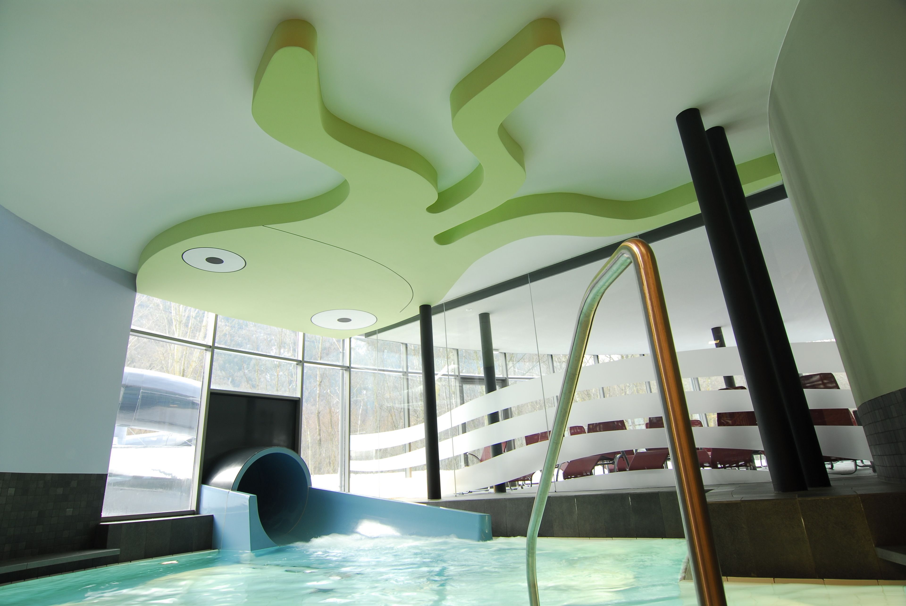 An indoor swimming pool with a slide, a metal ladder, and a modern ceiling design.