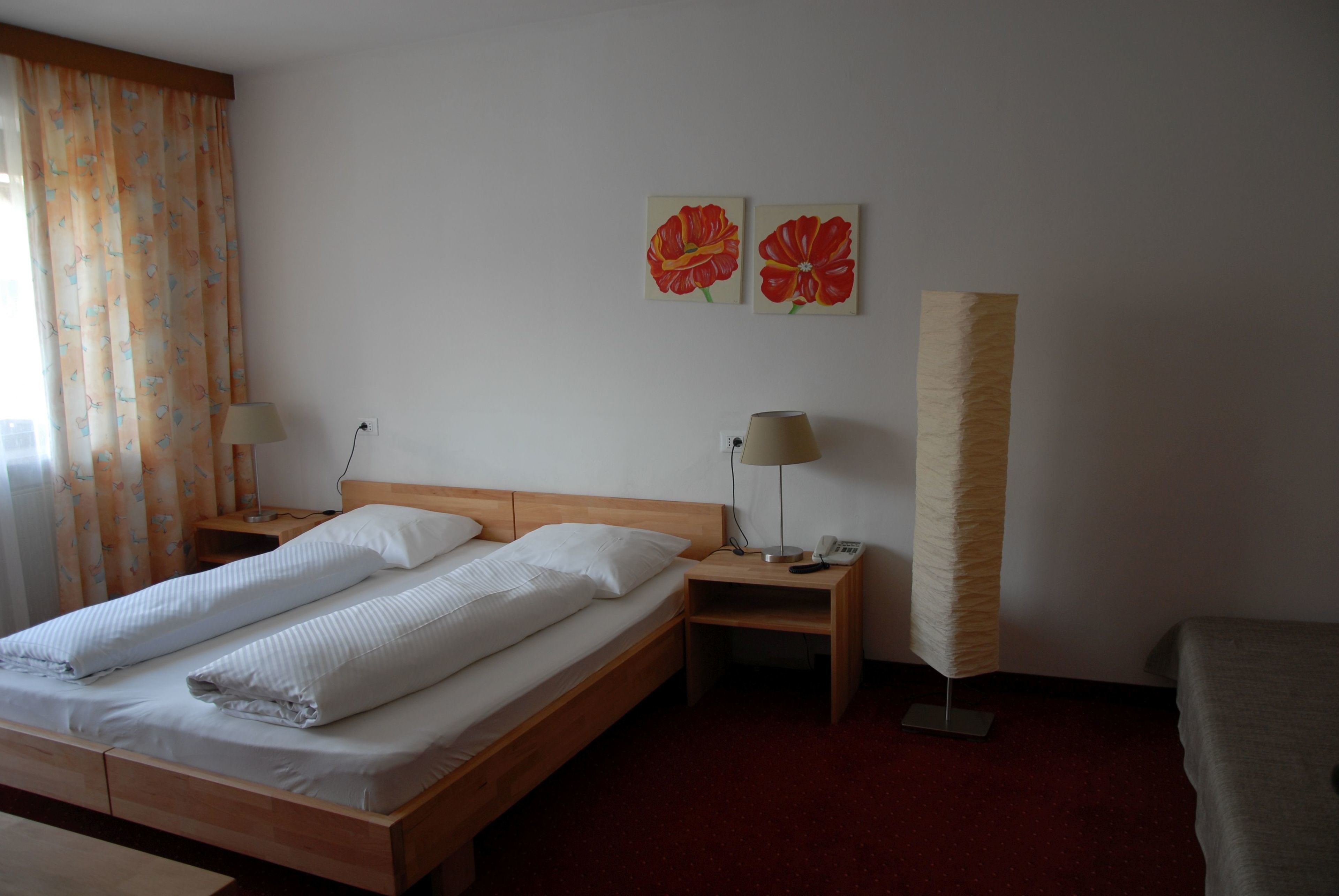Una camera d'albergo con un letto in legno, due comodini, una lampada e due quadri floreali al muro.