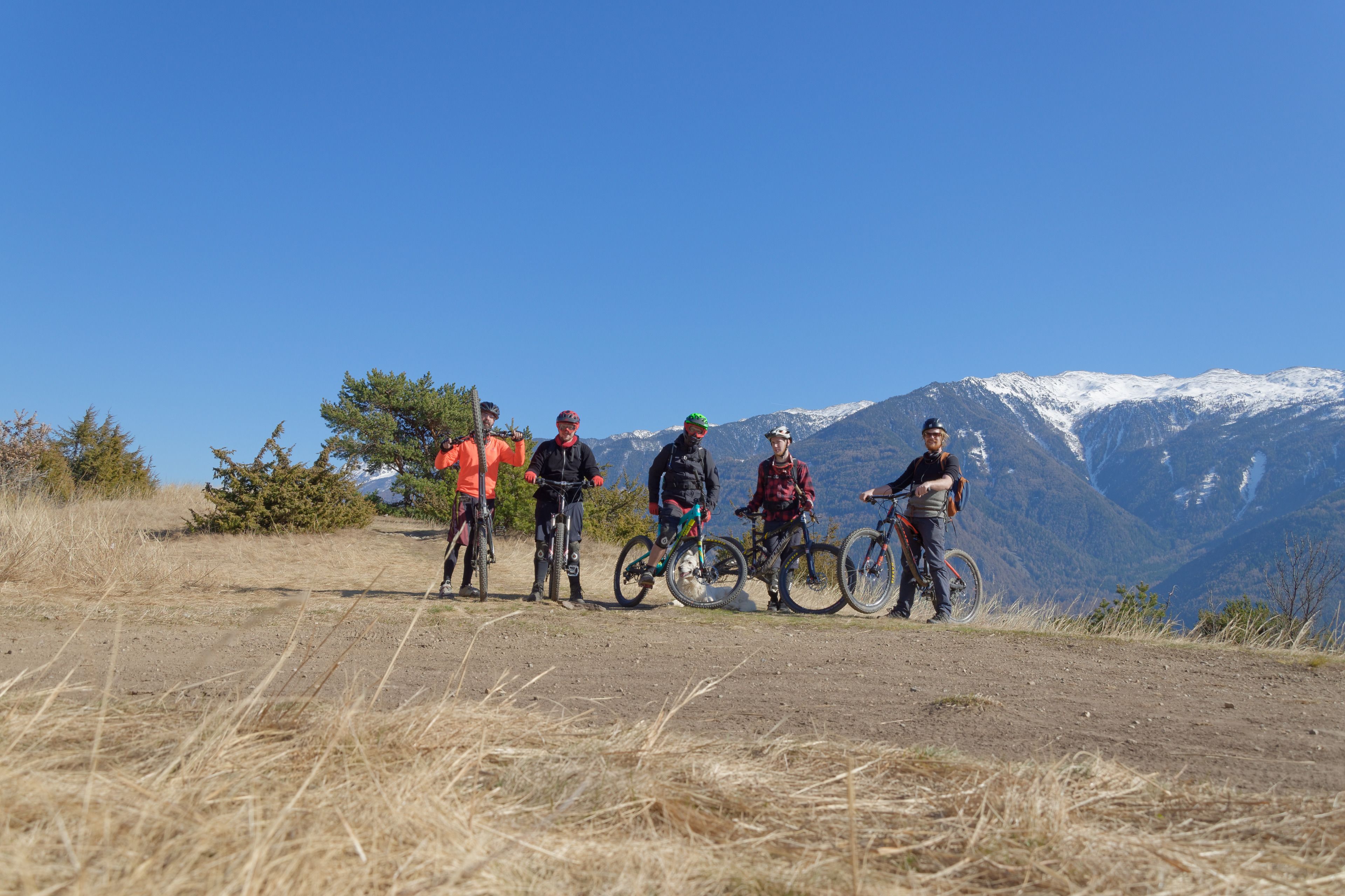 A group of people standing on a dirt path with bicycles, with a mountainous landscape in the background.