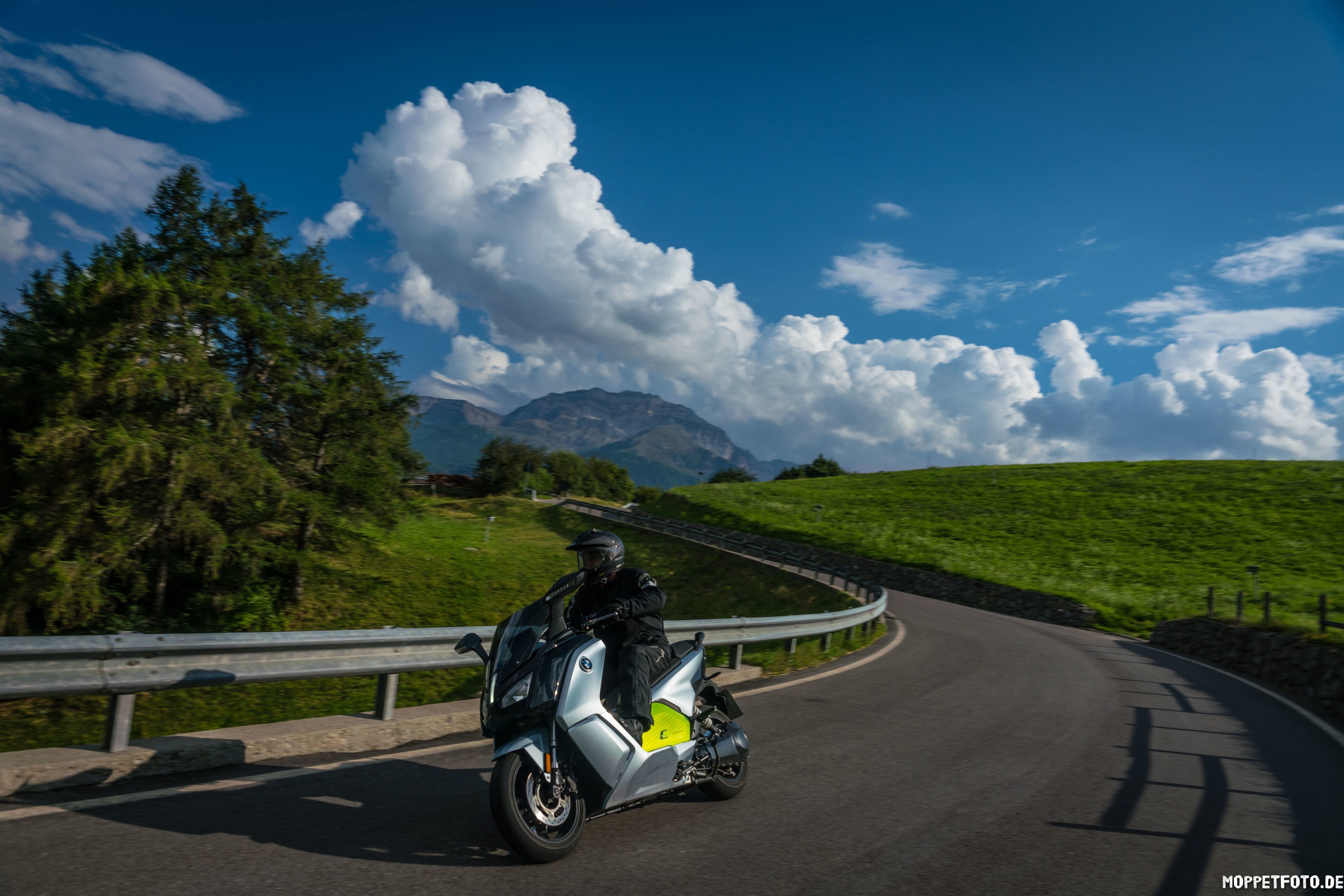 Un motociclista en una carretera sinuosa con una montaña al fondo.