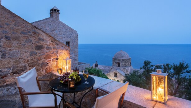 Un bâtiment en pierre avec une table et des chaises, une lanterne et une vue sur la mer.
