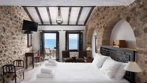 Une chambre avec un grand lit, une télévision, une table et des chaises. Il y a deux fenêtres donnant sur la mer.