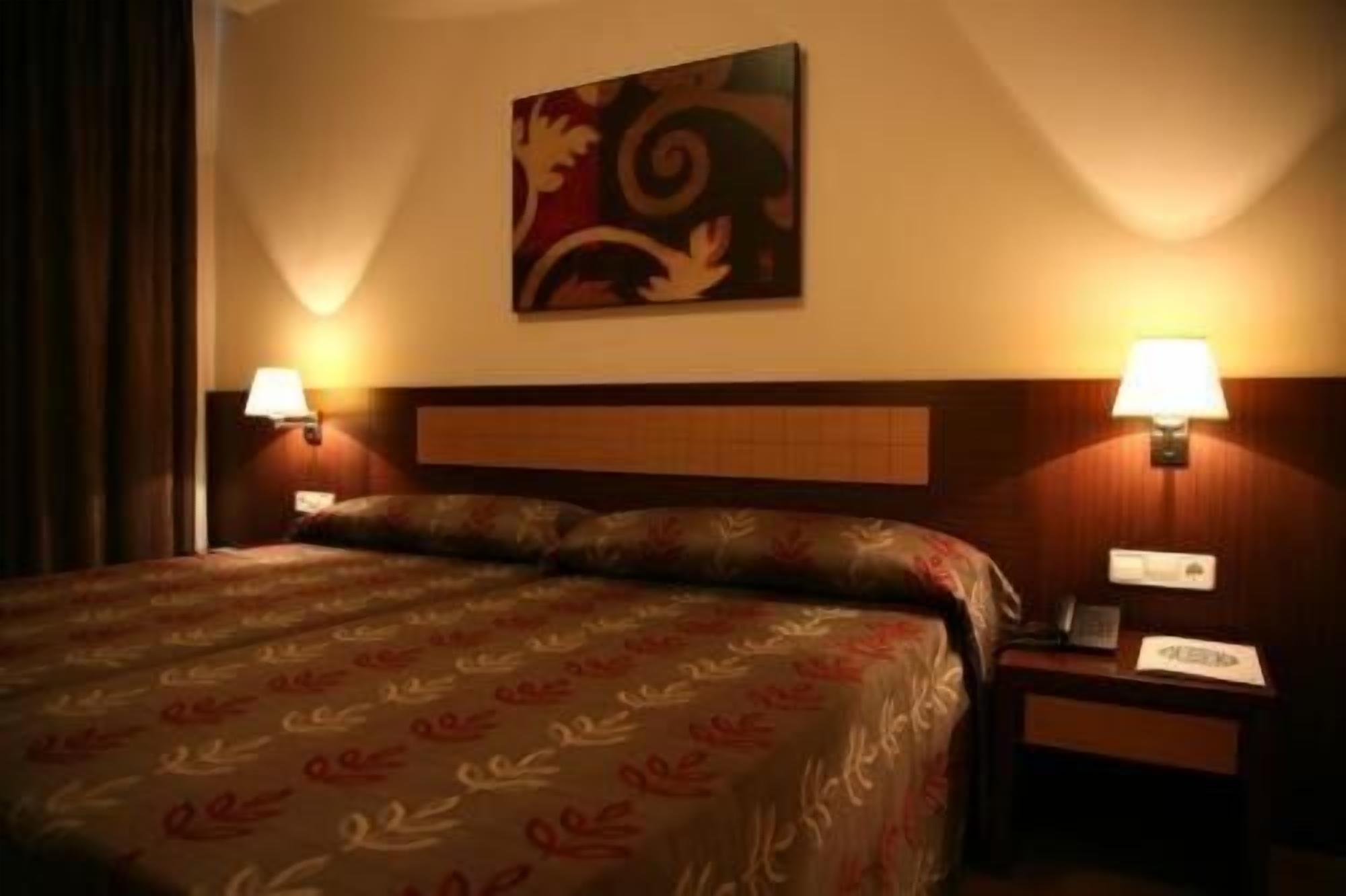 A hotel room with a bed, two bedside lamps, a nightstand, and a wall-mounted artwork.