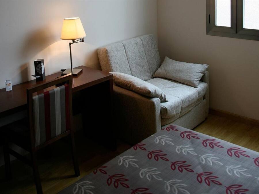 Ein kleiner, gemütlicher Raum mit einem Schlafsofa, einem Tisch mit einer Lampe und einem gemusterten Teppich.