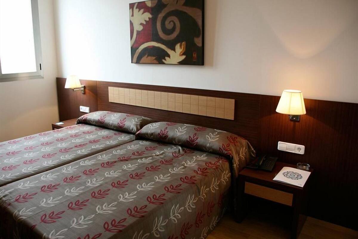 Habitación de hotel con una cama, dos mesitas de noche, una lámpara de pared y un adorno en la pared.