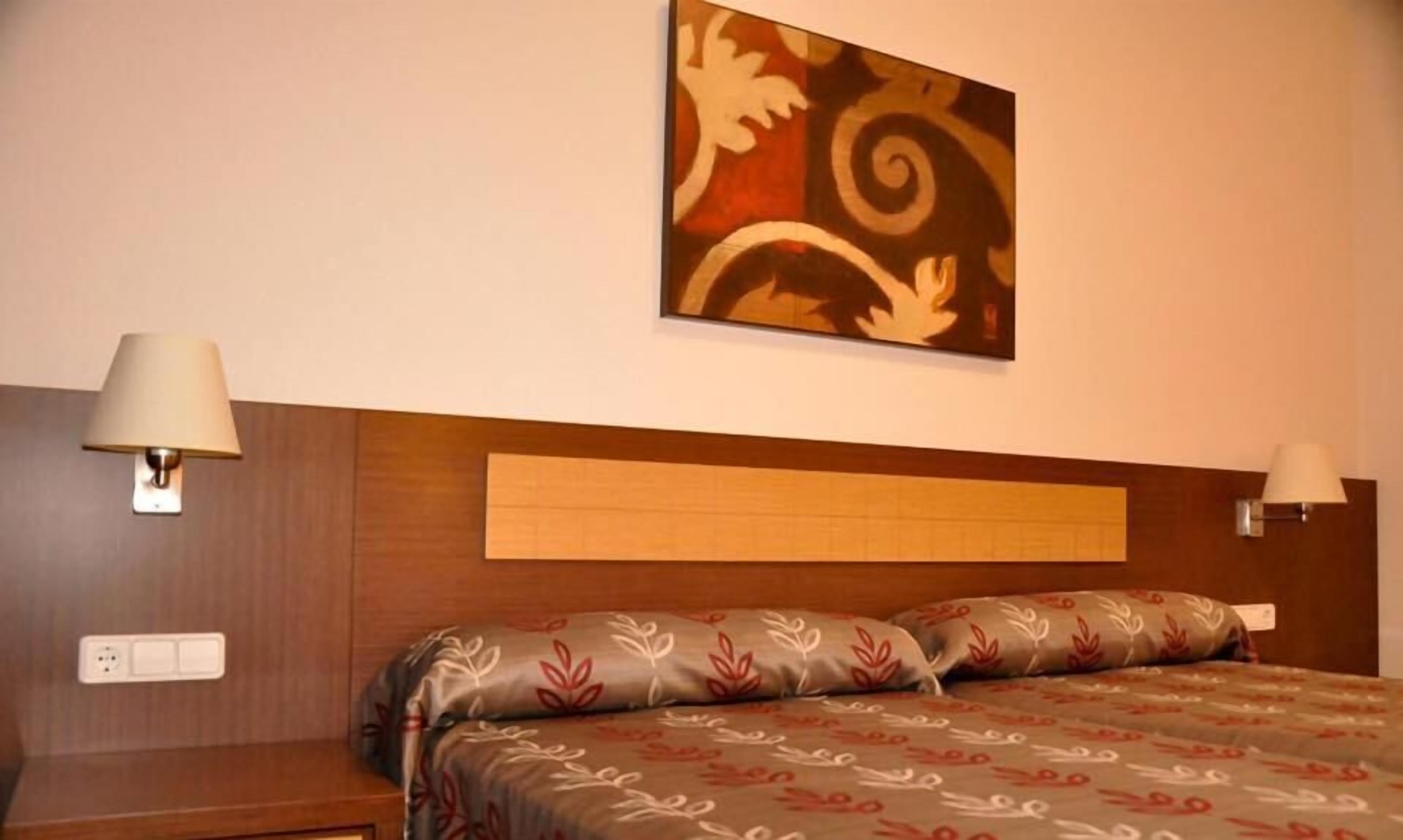 Ein Hotelzimmer mit einem Bett, zwei Nachttischlampen, einem Wandbild und einem Holzkopfstück.