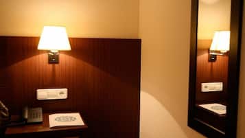 Une chambre d’hôtel avec une tête de lit en bois, une table de chevet avec une lampe, un téléphone et un miroir.