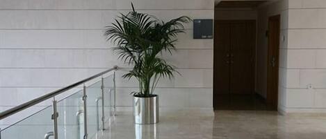 A hallway with a potted plant, a glass railing, and a door in the background.