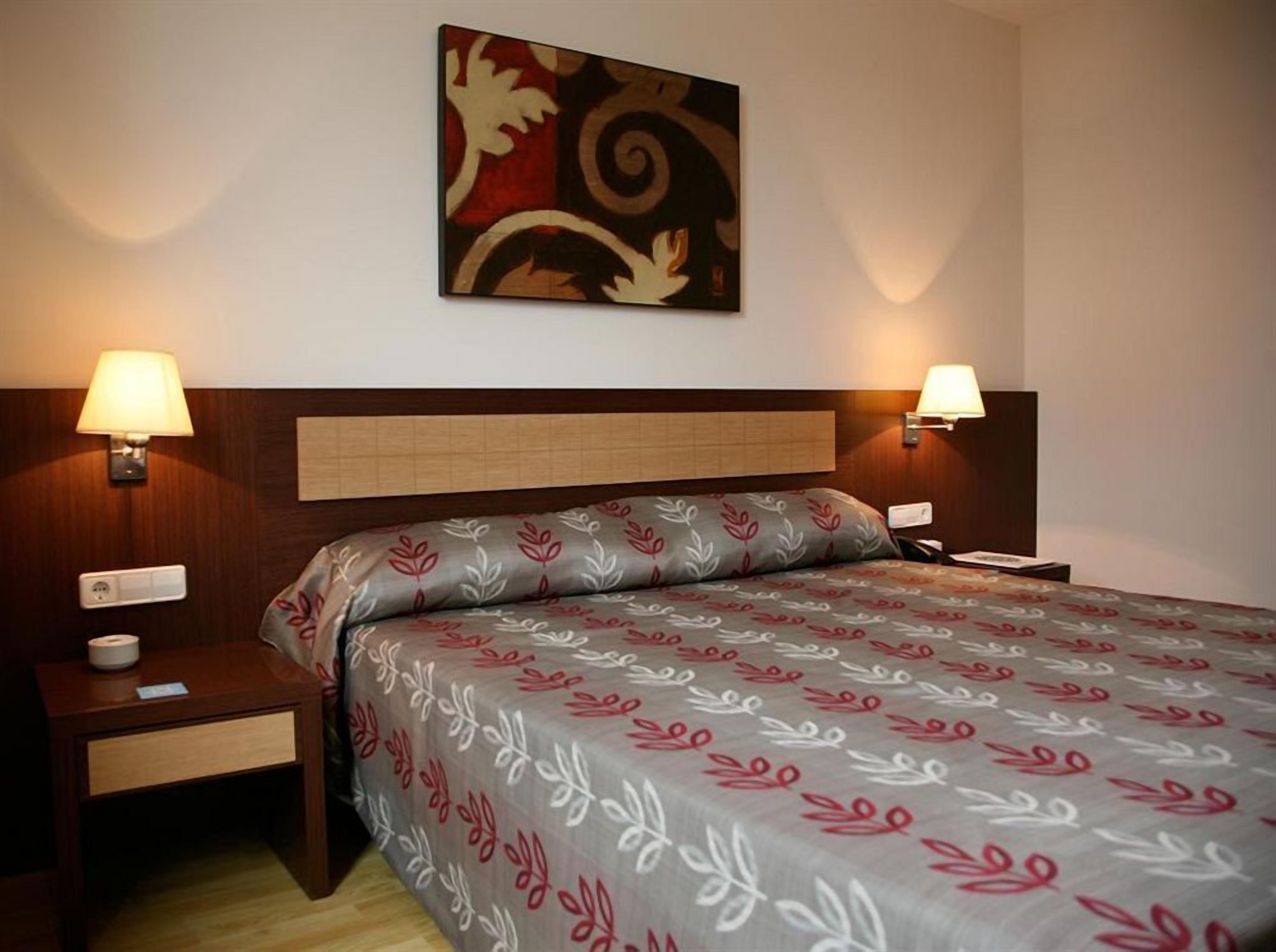 Habitación de hotel con cama, dos mesitas de noche, una obra de arte en la pared y dos lámparas de pared.