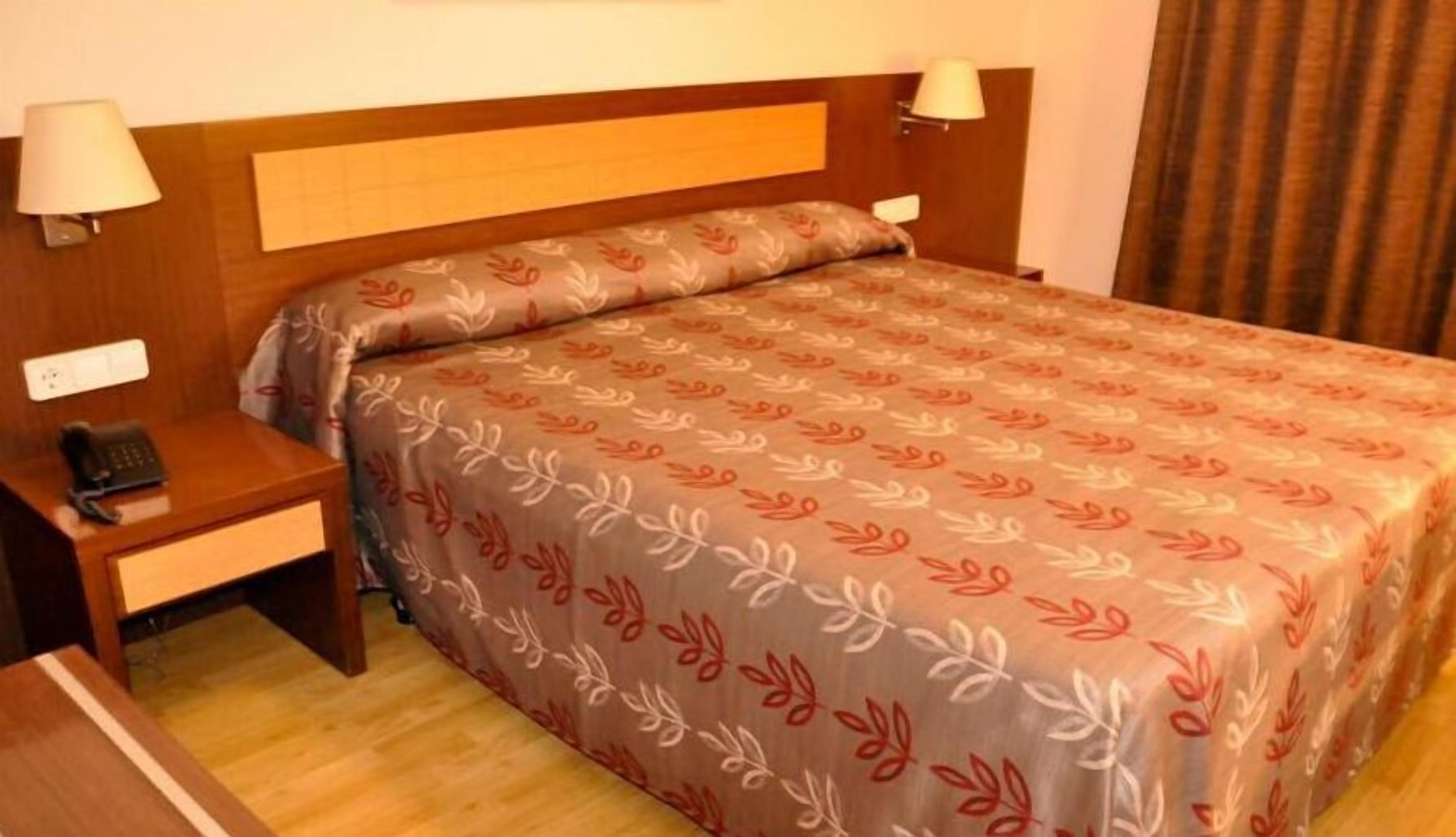 Una habitación de hotel con cama, mesita de noche, teléfono y dos lámparas de pared.