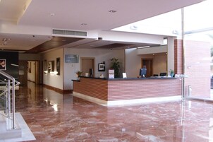 A hotel reception area with a marble floor, a reception desk, and a staircase leading to an upper level.