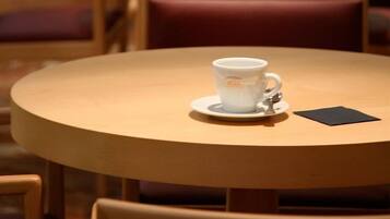 A round wooden table with a white ceramic cup and saucer, a black napkin, and a wooden chair.