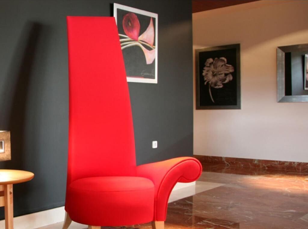 Una silla roja en un vestíbulo con pared oscura y suelo de mármol.