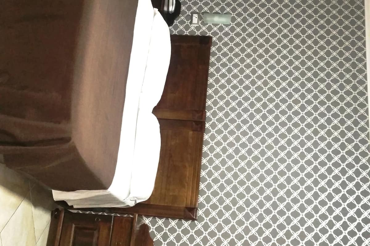 A room with a bed, a wooden nightstand, a patterned floor, and a ceiling light.