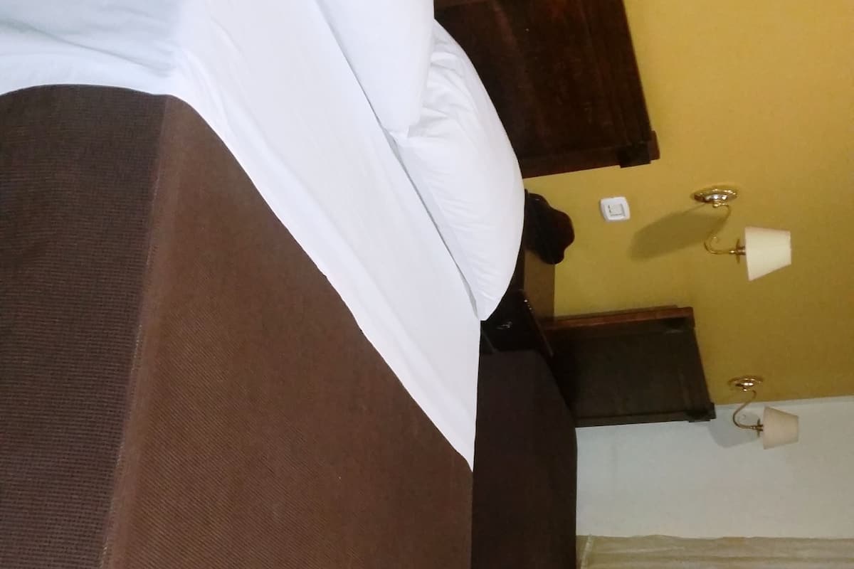 A bed with a brown headboard and white bedding in a room with yellow walls and wooden furniture.