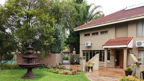 A building with a tiled roof, a fountain, and a well-maintained lawn. - Rusplek Guesthouse and Conference Centre (Bloemfontein)
