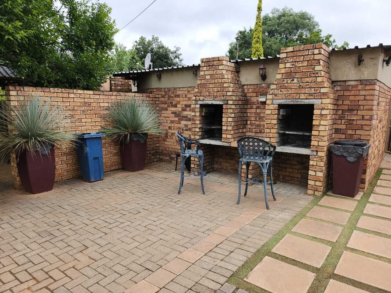 A brick outdoor kitchen with two barbecue grills, a seating area with two chairs, and potted plants.