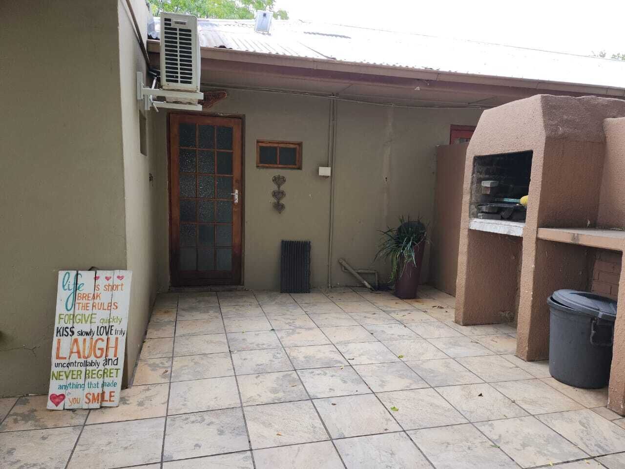 Un espacio exterior pequeño y cerrado con suelo de baldosas, una puerta, un ventanal y un cartel con frases motivacionales.