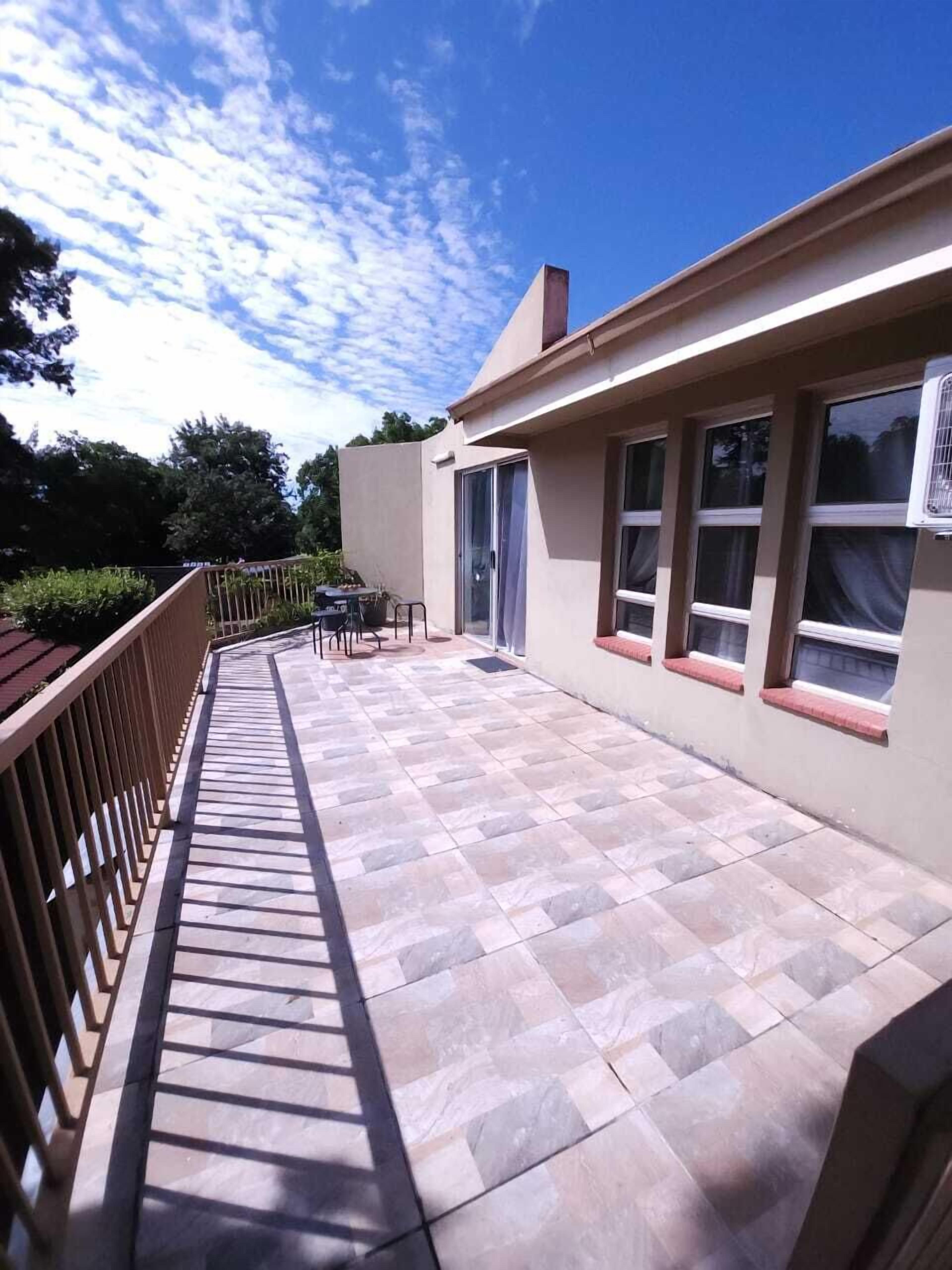 A covered patio with a tiled floor, a table and chairs, and a window with an air conditioning unit.