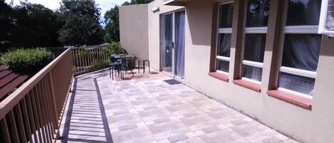 A covered patio with a tiled floor, a table and chairs, and a window with an air conditioning unit.