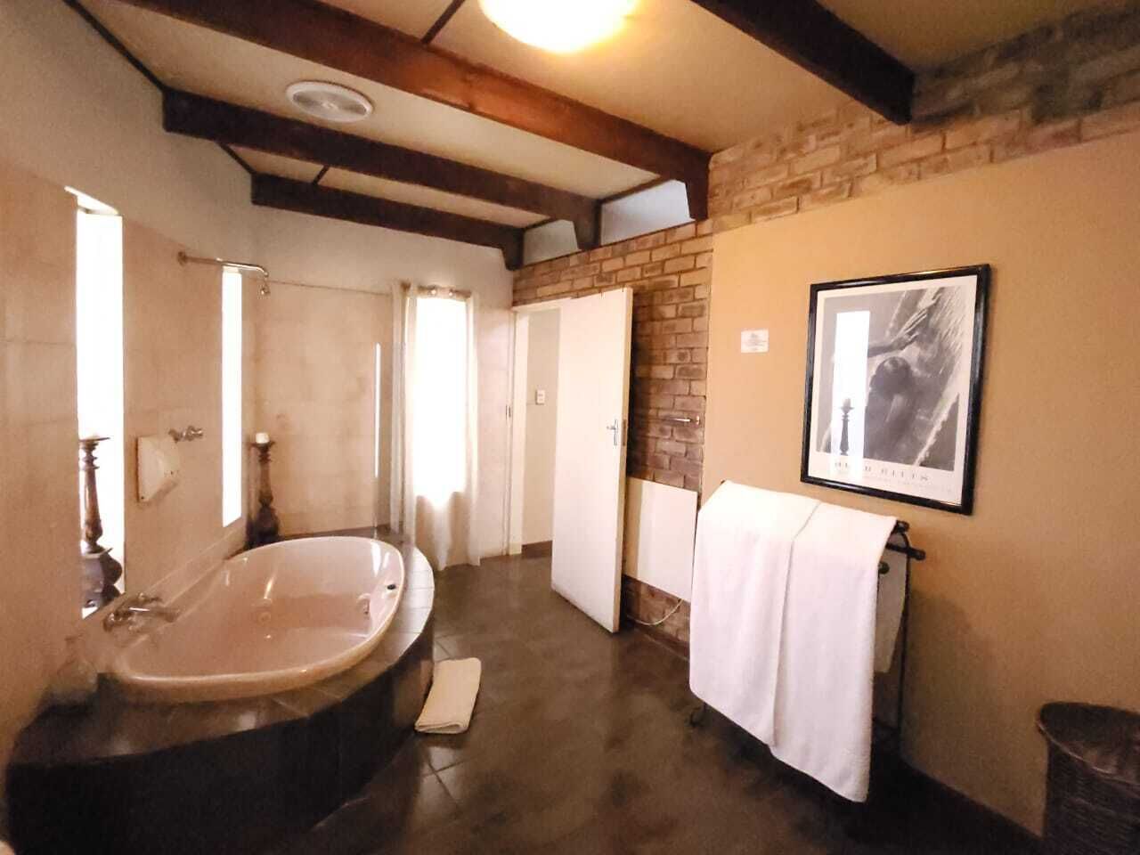 Un baño con una bañera grande, un espejo, un perchero para toallas y un cuadro en la pared.