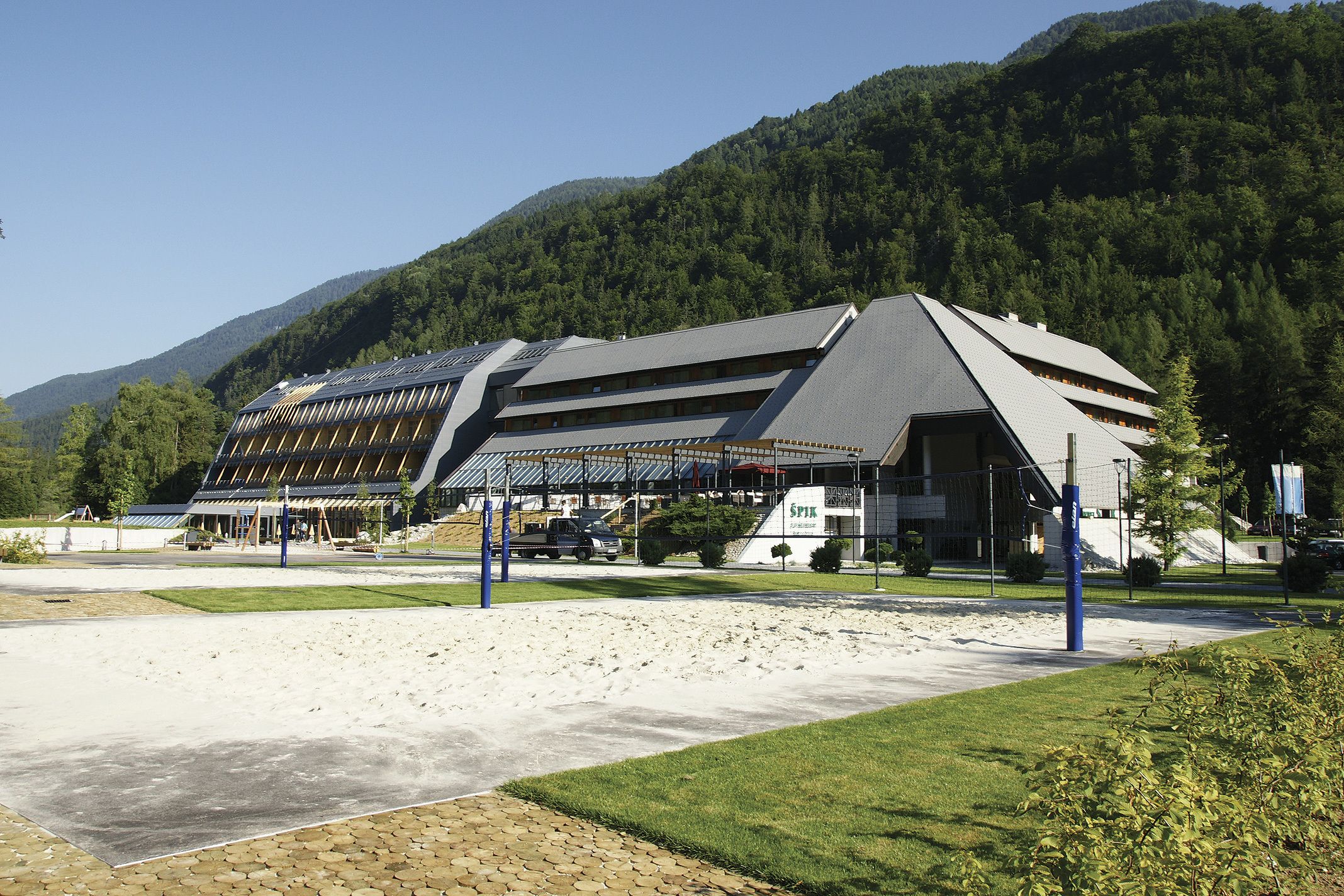 Un bâtiment moderne doté d’un toit en pente, de grandes fenêtres et d’un espace de stationnement à l’avant.
