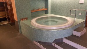 Una bañera de hidromasaje circular con recinto de vidrio, rodeada de suelo de baldosas y un estante de madera con velas.