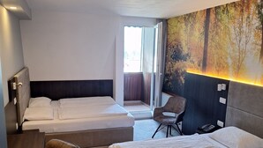 Habitación de hotel con dos camas, un escritorio, una silla y un ventanal grande.