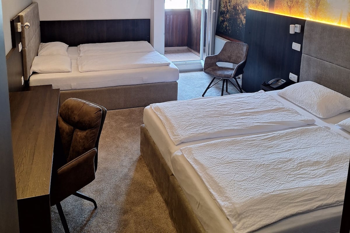 A hotel room with two beds, a desk, a chair, and a large window.