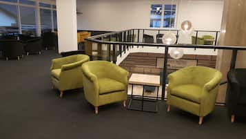 Een moderne spa-ruimte met groene fauteuils, een houten tafel en een glazen balustrade.