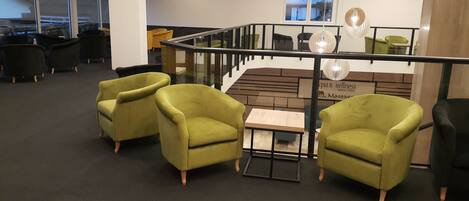A modern spa area with green armchairs, a wooden table, and a glass railing.