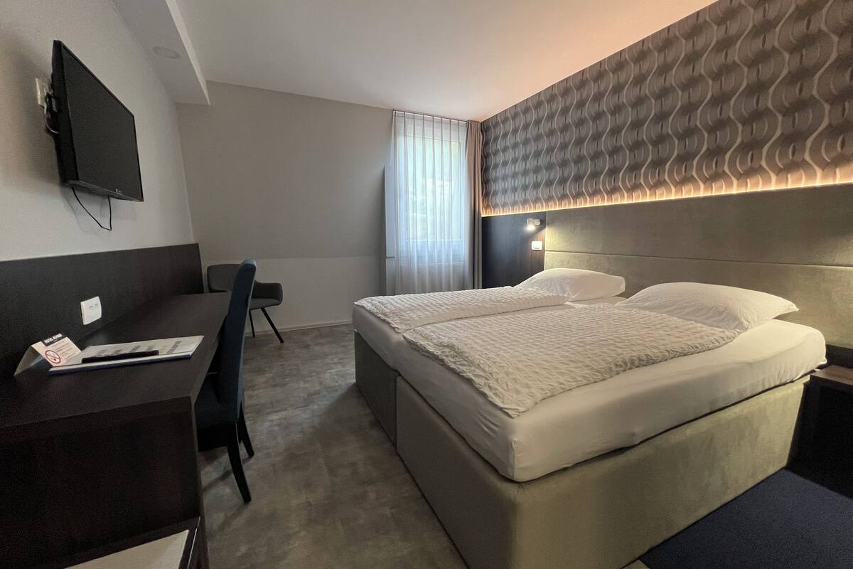 A hotel room with a bed, a desk, a chair, a television, and a window with curtains.