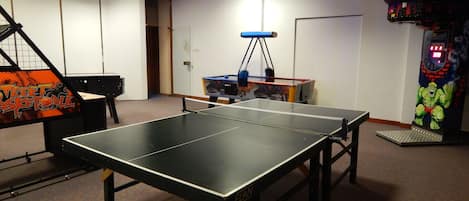A ping pong table in a room with a basketball arcade, a claw machine, and a door leading to another room.