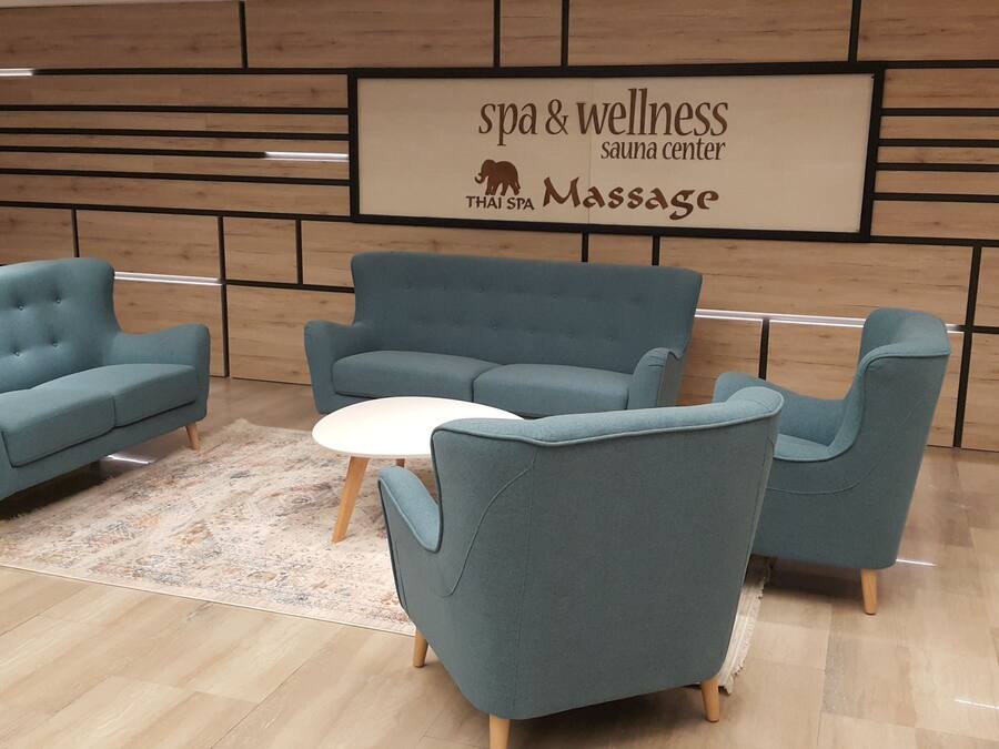 Un centro benessere e spa con un cartello che recita “spa & wellness sauna center THAI SPA Massage”. Sono presenti tre poltrone blu e un tavolo rotondo bianco al centro.