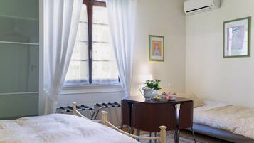 Une chambre d’hôtel avec deux lits, une petite table avec une plante et une fenêtre avec des rideaux.