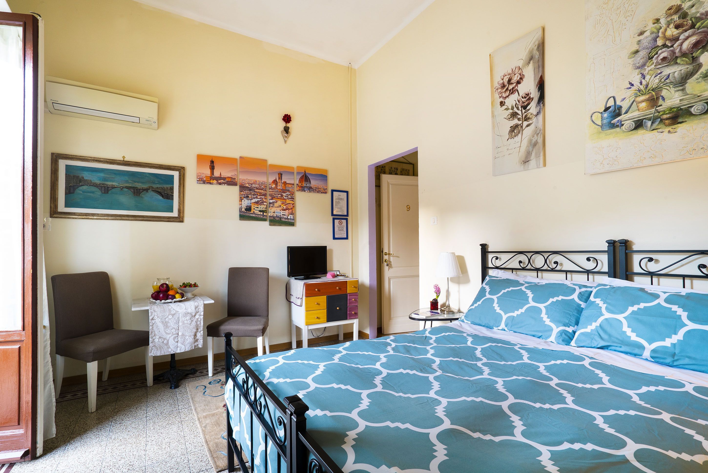 Un dormitorio con una cama, un escritorio con una computadora, una silla y una mesita con un cuenco de fruta.