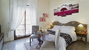 A hotel room with a bed, a small table with a lamp, a chair, and a window with curtains. - 1900 Artevita (Florence)