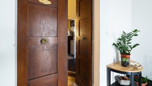 A wooden door with a brass handle and a brass plate, leading to a hallway with a potted plant on a small table. - 1900 Artevita (Florence)