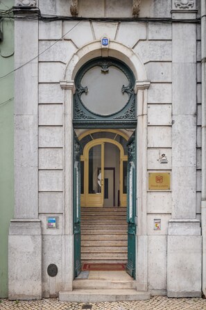 A building entrance with a stone facade, a green door, and a staircase leading inside. - Pensão Londres (Lisbon)