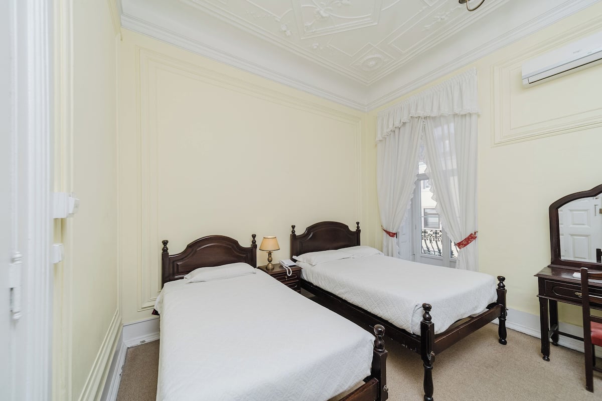 A hotel room with two single beds, a wooden dresser, a mirror, and a window with white curtains.