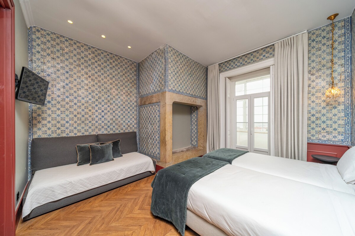 A hotel room with two beds, a fireplace, a TV, and a large window.