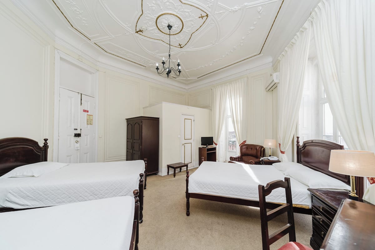 A hotel room with two beds, a chandelier, a wardrobe, a desk, and a chair.