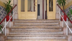 A grand staircase with a marble finish leading to a yellow door with glass panels, flanked by white railings and potted plants. - Pensão Londres (Lisbon)